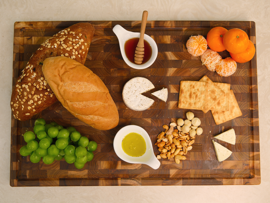 End-grain teak cutting board serving bread, grapes, cheese and honey