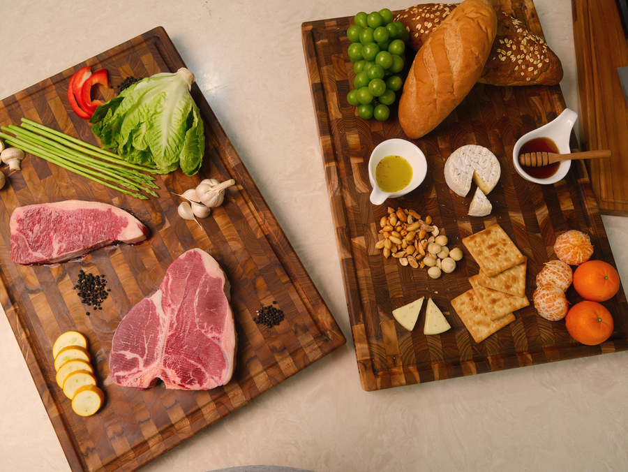 Two end-grain teak cutting boards with steak, vegetables and a grazing spread