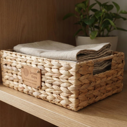 Small basket on a shelf holding folded linens beside a potted plant