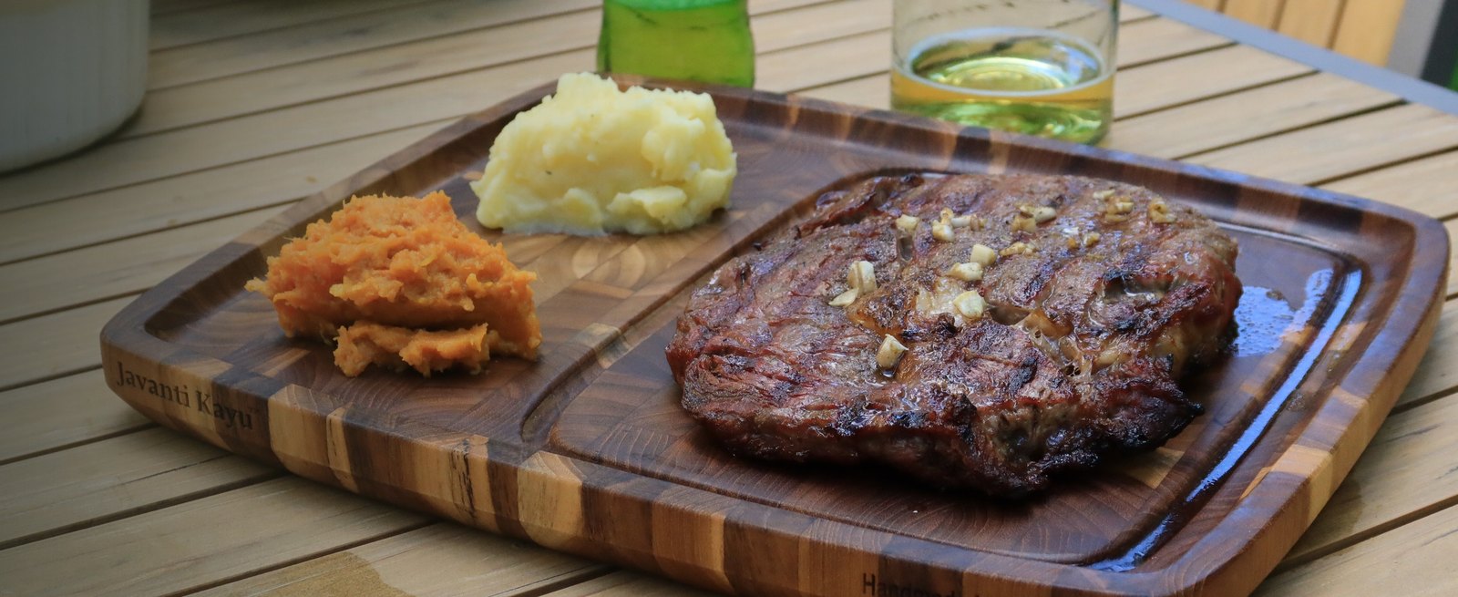 Grilled ribeye with sides resting on an end grain teak steak plate